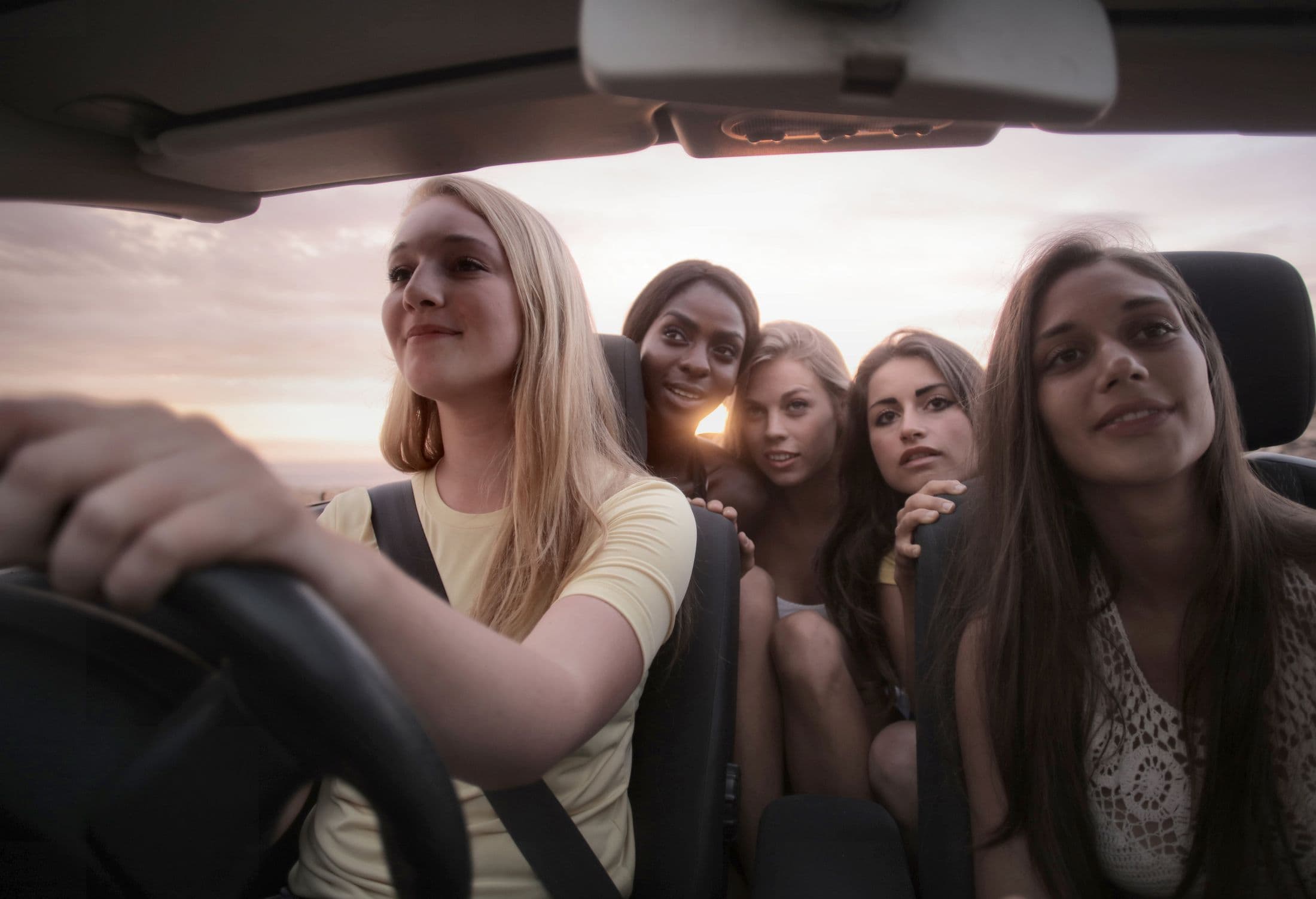 A group of friends travelling together in an open car at sunset